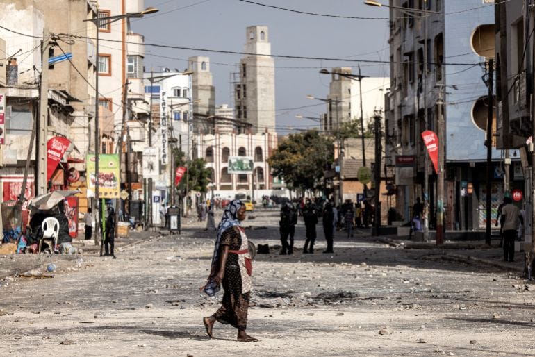 Stones and debris are seen in a street in Dakar as a woman crosses the street in the aftermath of a protest. Stones and debris are seen in a street in Dakar as a woman crosses the street in the aftermath of a protest.