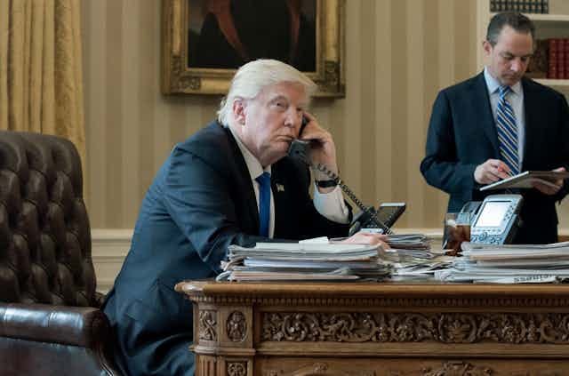 Donald Trump on the telephone in the Oval Office with an aide in the background, January 2017. Donald Trump on the telephone in the Oval Office with an aide in the background, January 2017.
