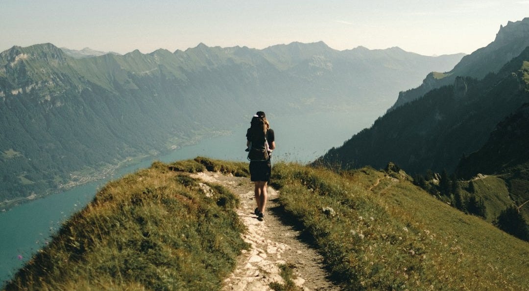 person hiking above mountain overlooking river