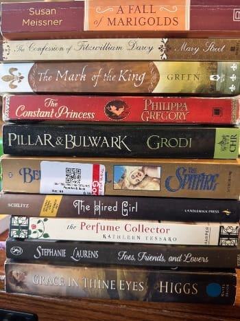Stack of historical romance novels on top of a dark wood table, stacked in random order