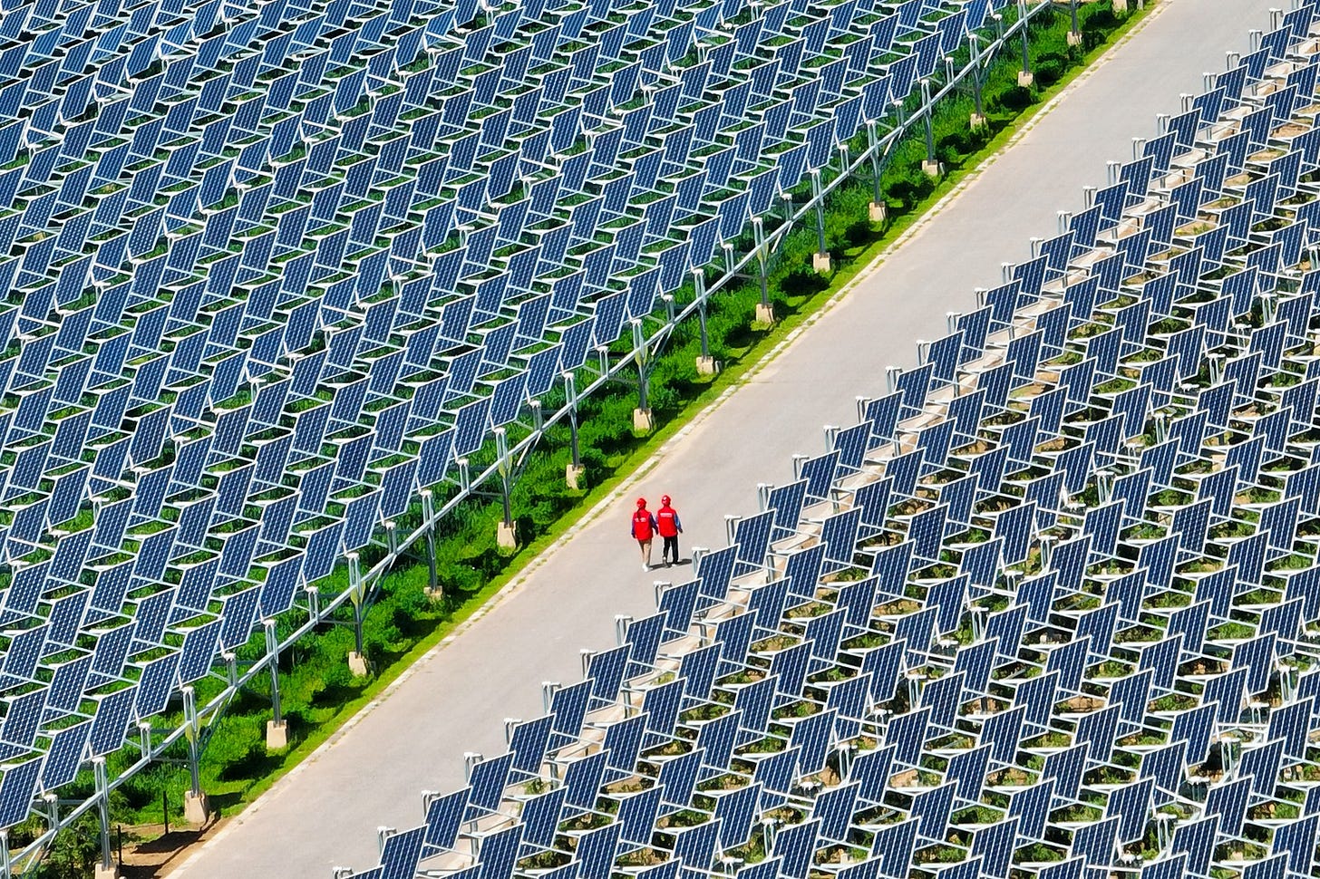 Two workers walk on a path among grids of many solar panels. Two workers walk on a path among grids of many solar panels.