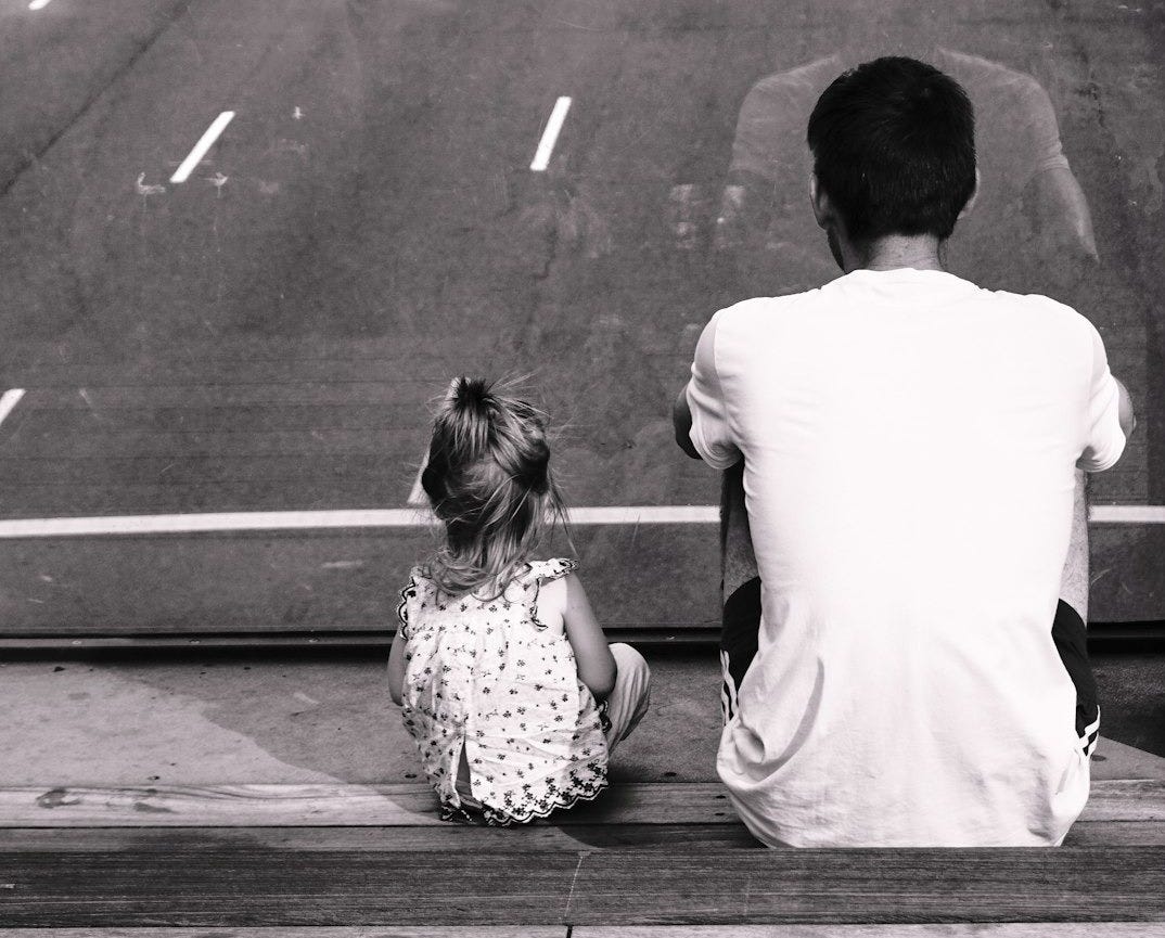 grayscale photography of man and girl sitting on staircase fronting road with passing cars