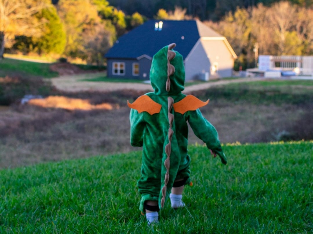 boy in green and orange jacket walking on green grass field during daytime