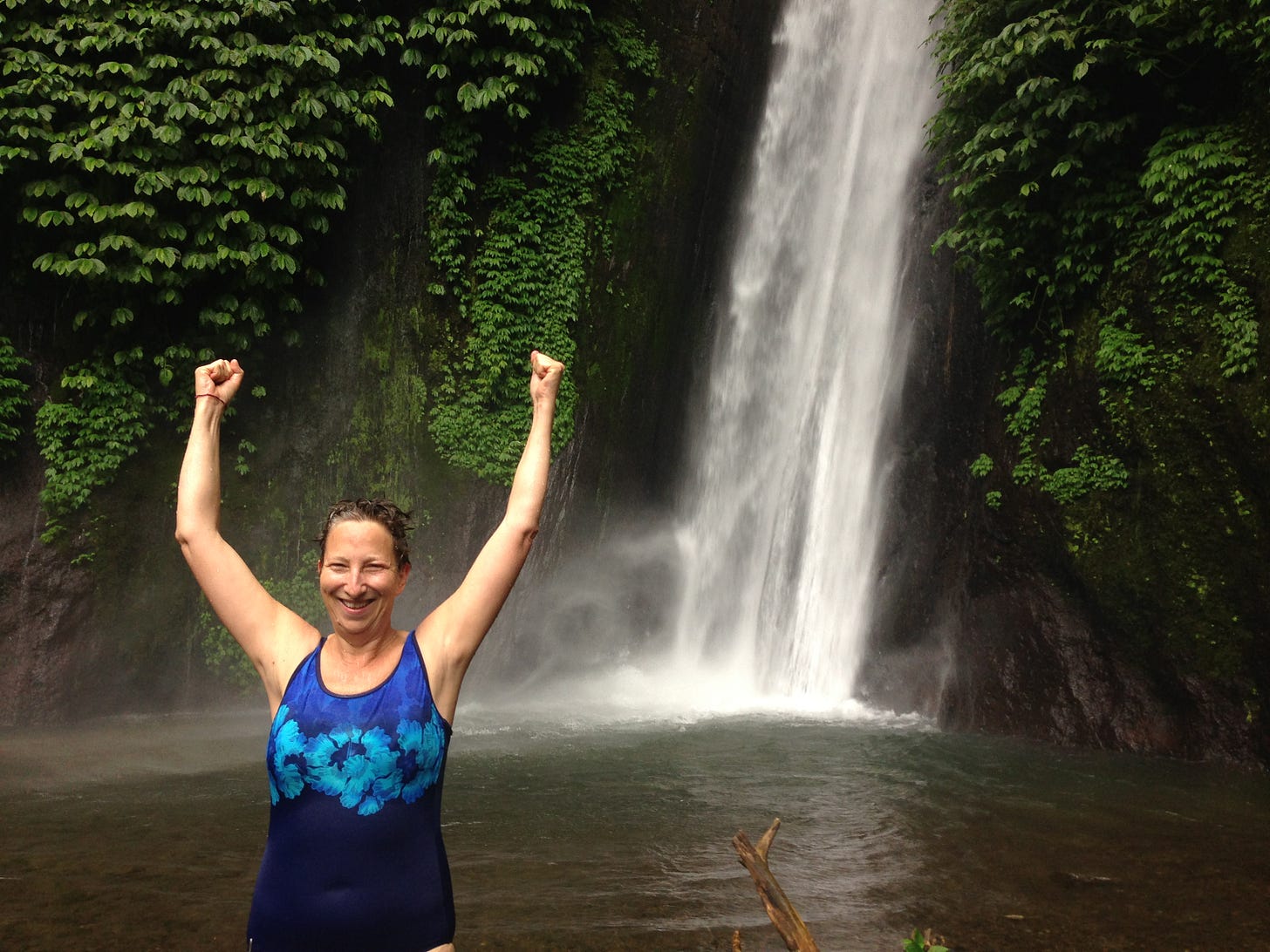 hands raising in celebration in front of a waterfall in Bali