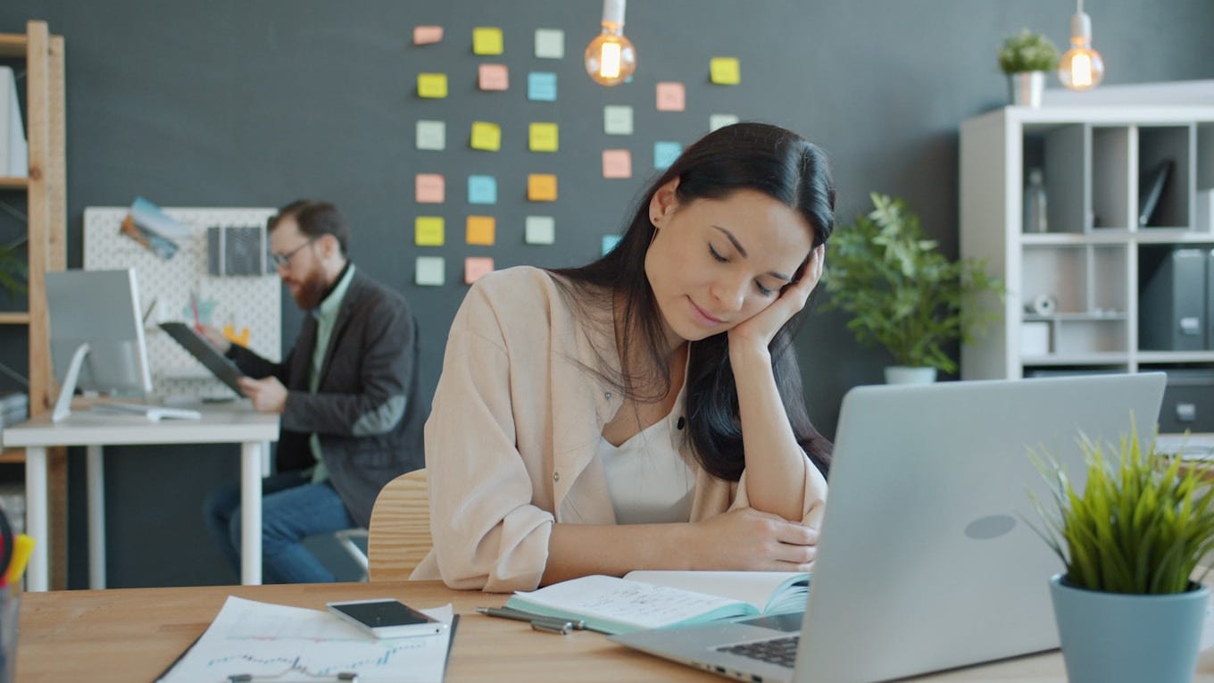 A product manager resting her head on her hand at a busy desk