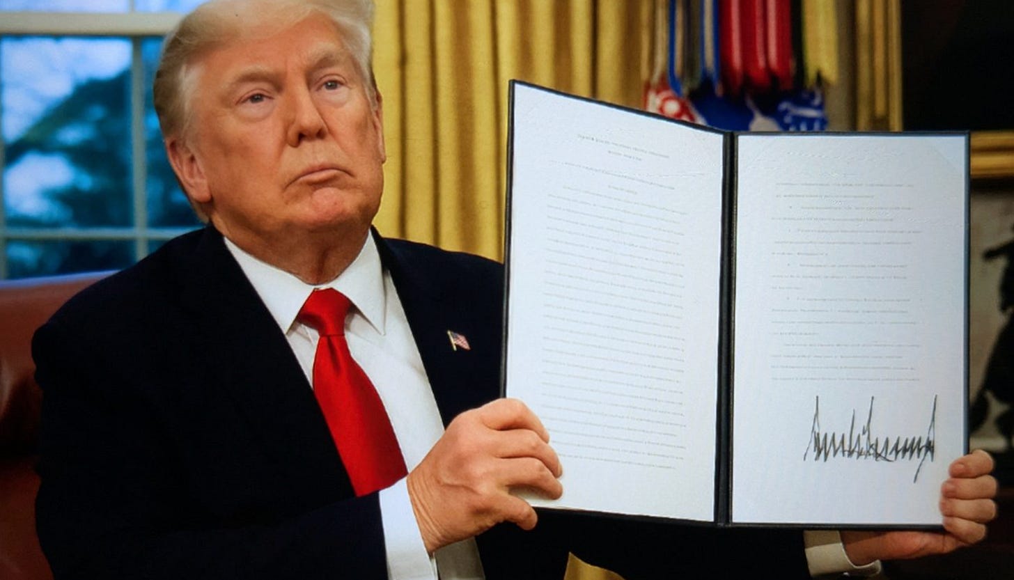 President Trump holding up a signed executive order document in the Oval Office