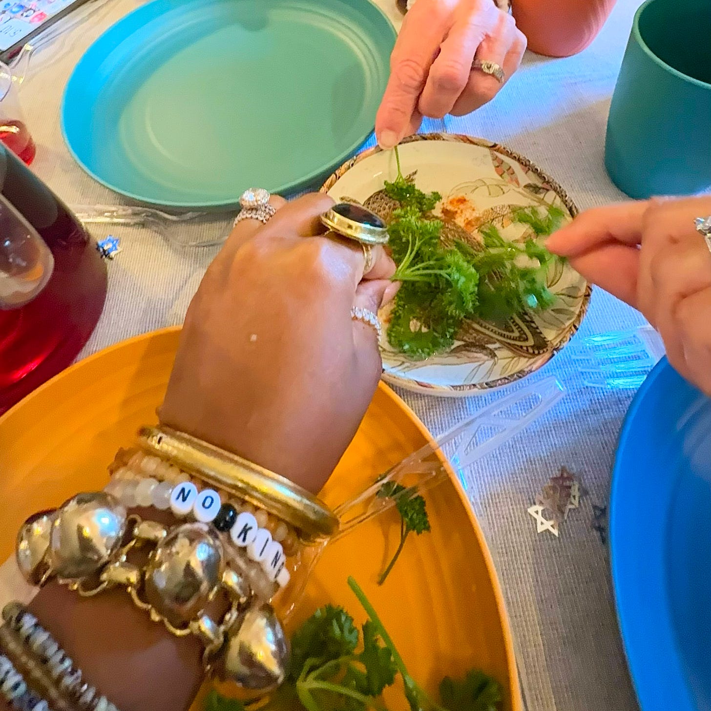 Hands holding fresh herbs over a Seder plate during a Passover ritual, symbolizing participation, learning, and connection through Jewish ceremonial food traditions.