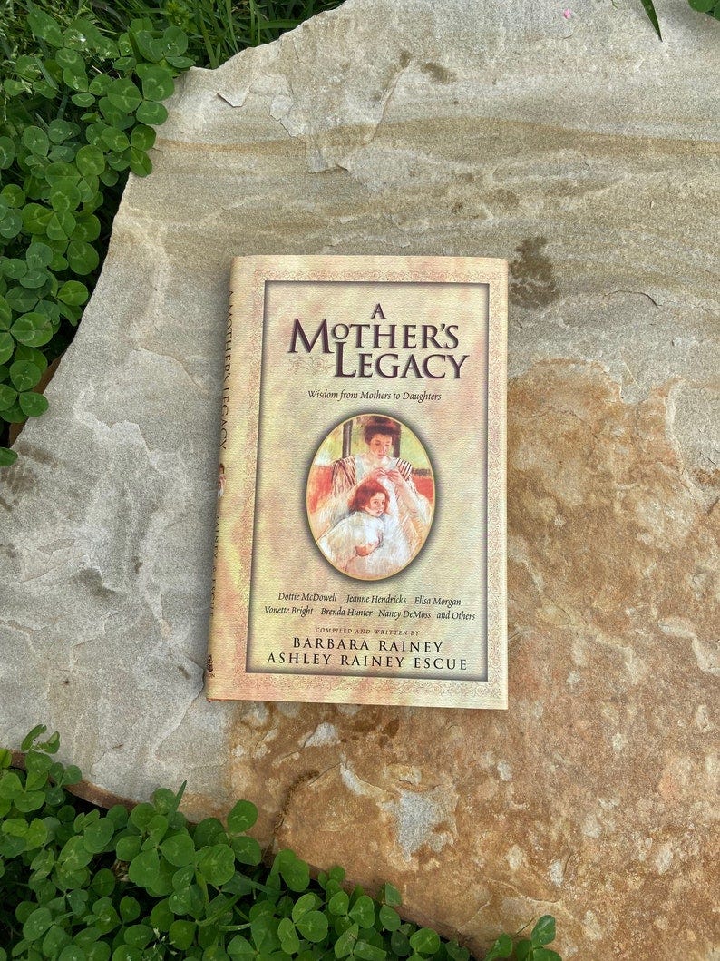 May include: A Mother's Legacy book cover with a yellow background and a picture of a mother and child. The book title is 'A Mother's Legacy' and the subtitle is 'Wisdom from Mothers to Daughters'. The book is written by Barbara Rainey and Ashley Rainey Escue.