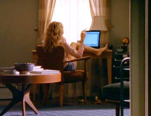 This may contain: a woman sitting at a table with a laptop computer in her lap looking out the window