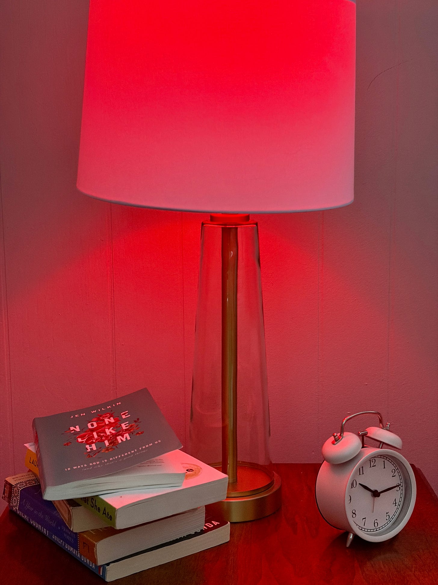 red light bulb in lamp with books and a clock on the night stand