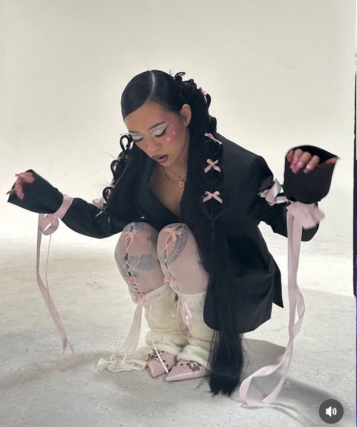 This may contain: a woman kneeling on the ground with her hands in her pockets and holding two pink ribbons