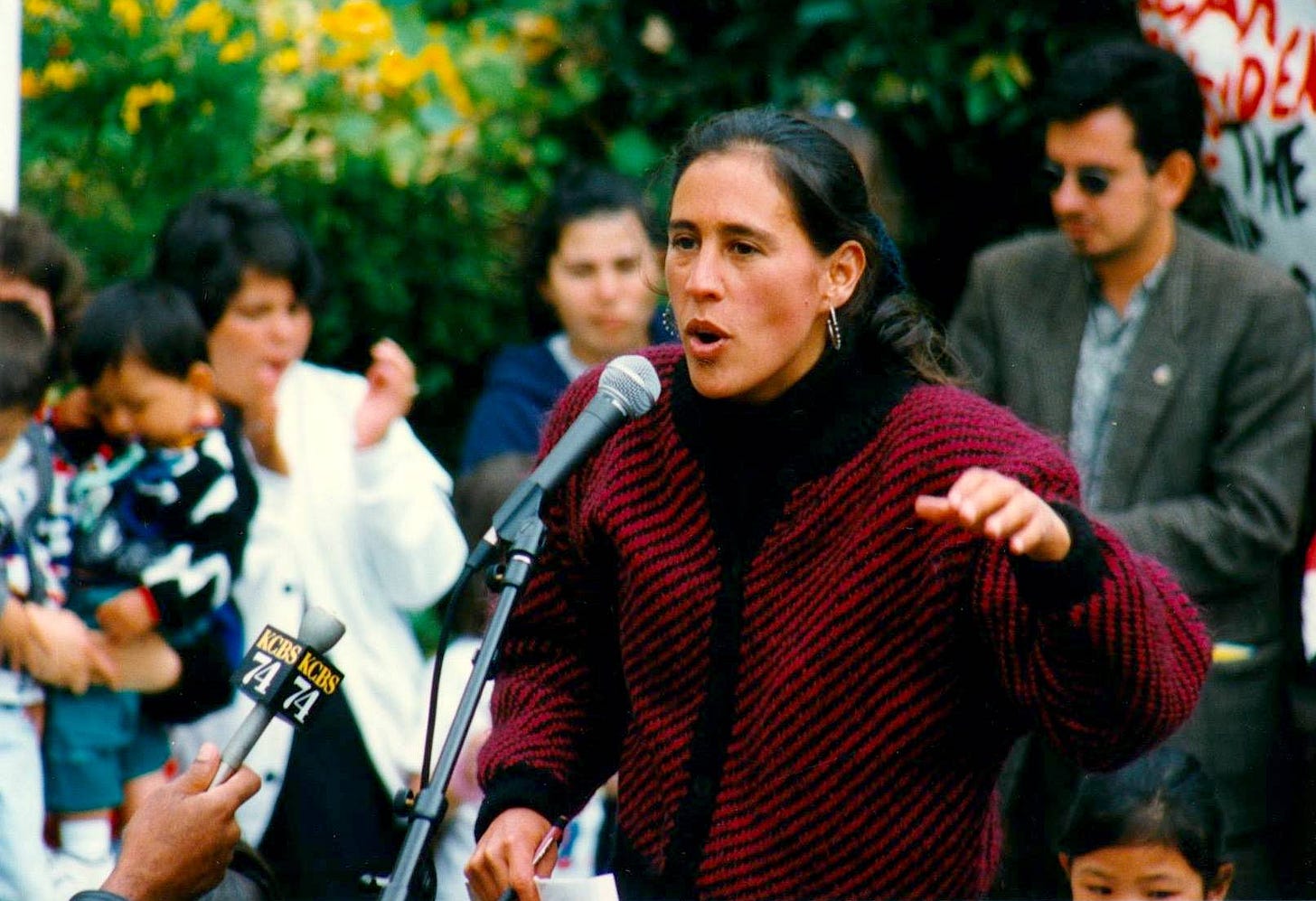 Julie speaking on the mic at an outdoor rally.