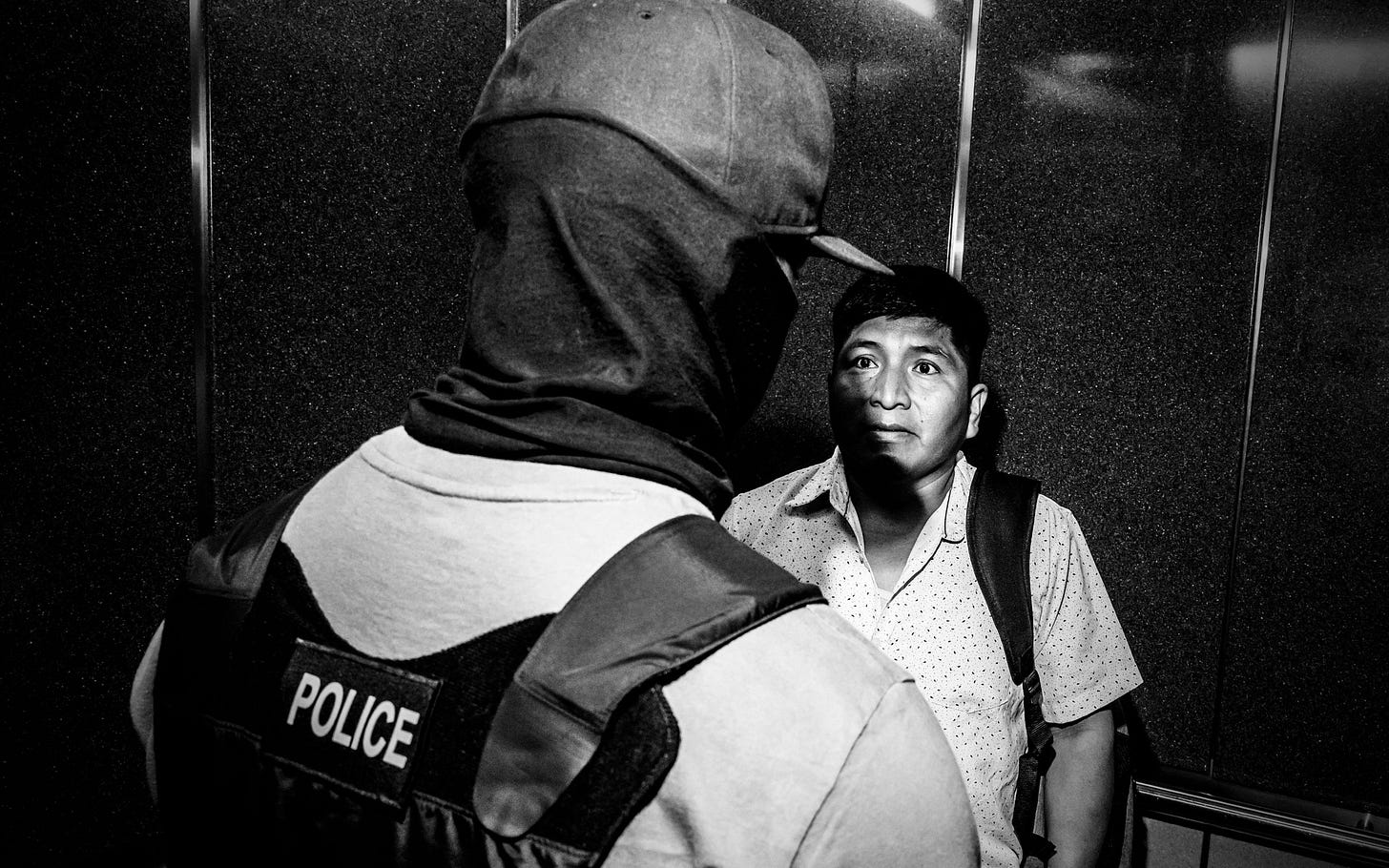 A man wearing a police vest looms over another man. A man wearing a police vest looms over another man.