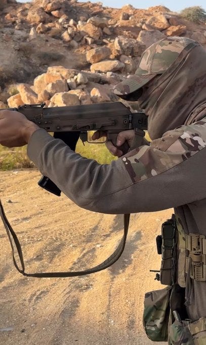 First image shows a person in camouflage clothing and hood holding an AK-style rifle while aiming in a rocky desert terrain with boulders and sand. Second image depicts a person in tactical vest and balaclava standing indoors holding a rifle with gear pouches and straps attached to clothing.