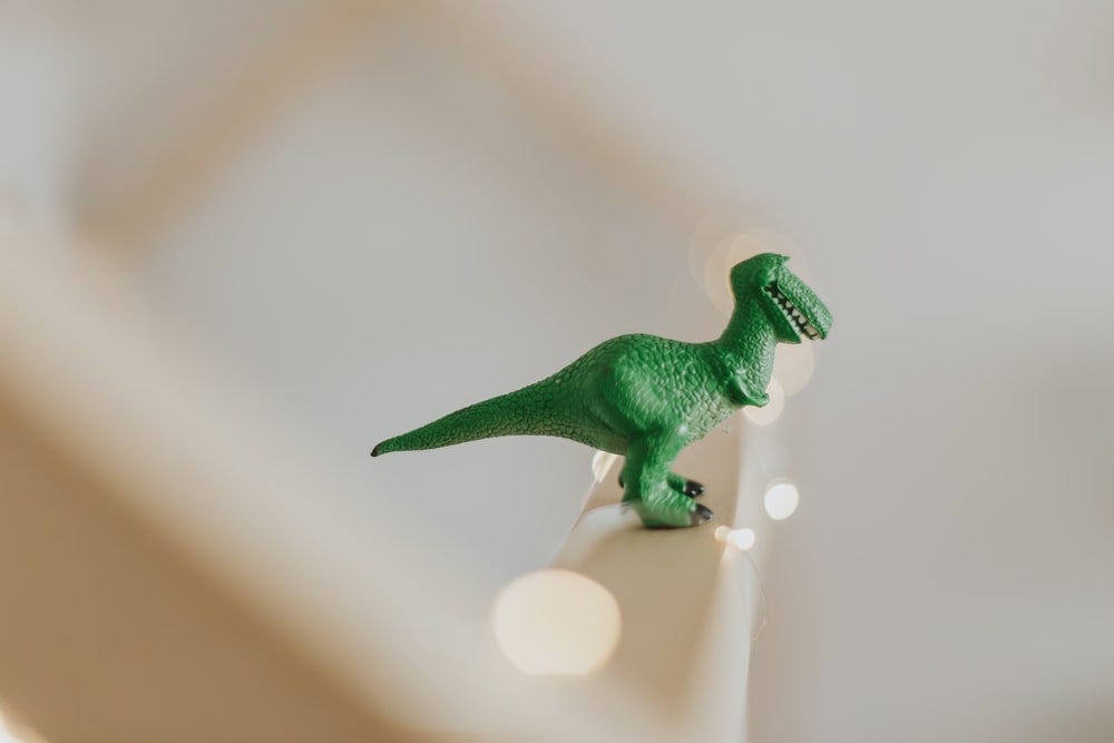 green T-rex toy on white stair green T-rex toy on white stair