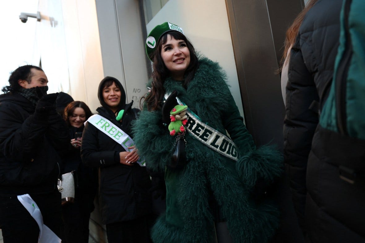 Supporters of Luigi Mangione gather outside Manhattan Criminal Court, with one woman wearing a "FREE LUIGI" sash.