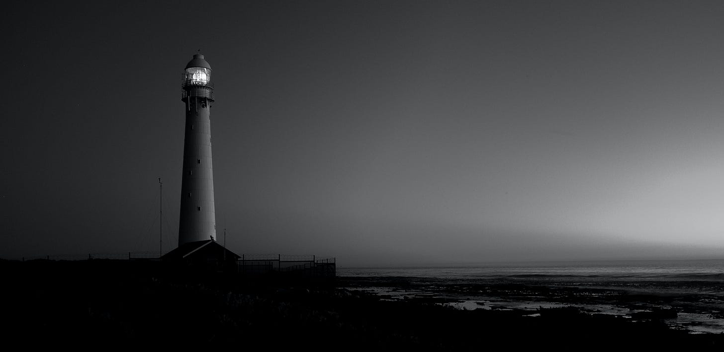 A lighthouse shines over a dark coastline