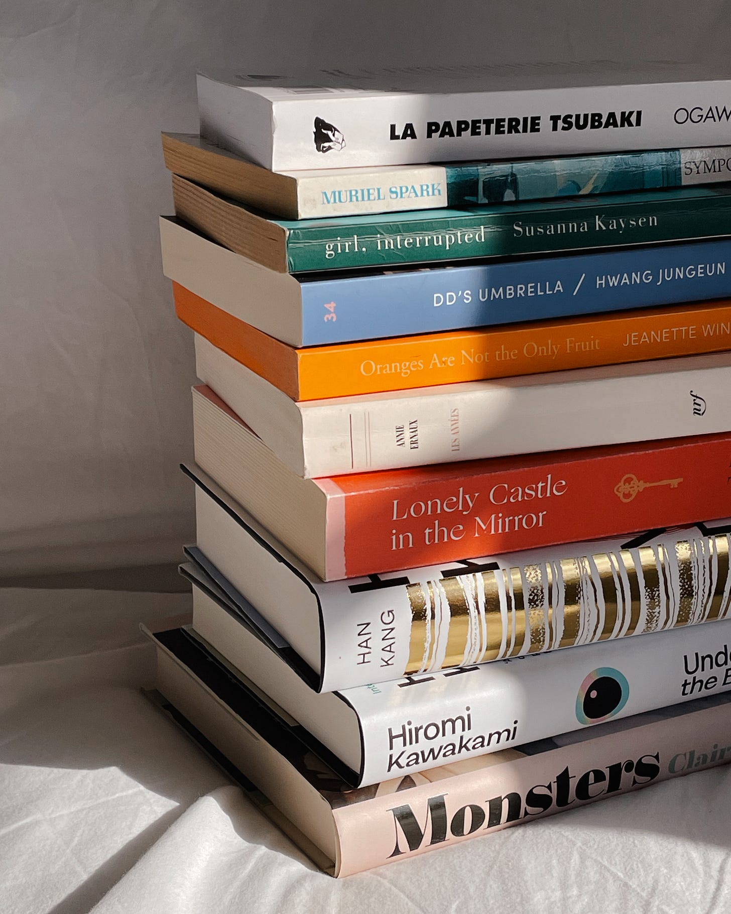 A neatly stacked pile of my spring tbr on white bedding, bathed in soft sunlight and gentle shadows.