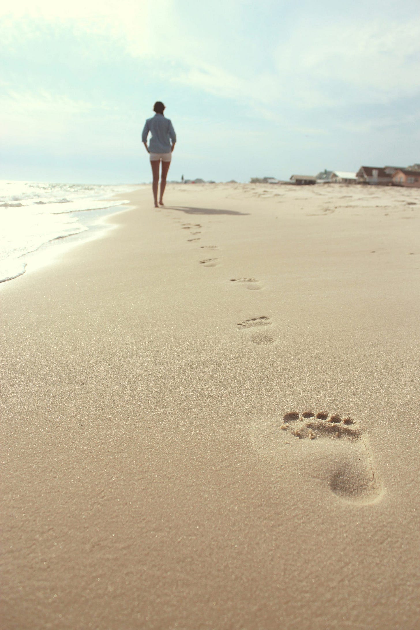 A woman walking alone on the beach, leaving footprints in the sand, symbolizing the journey of self-reflection and allowing others to show who they truly are, rather than holding onto expectations