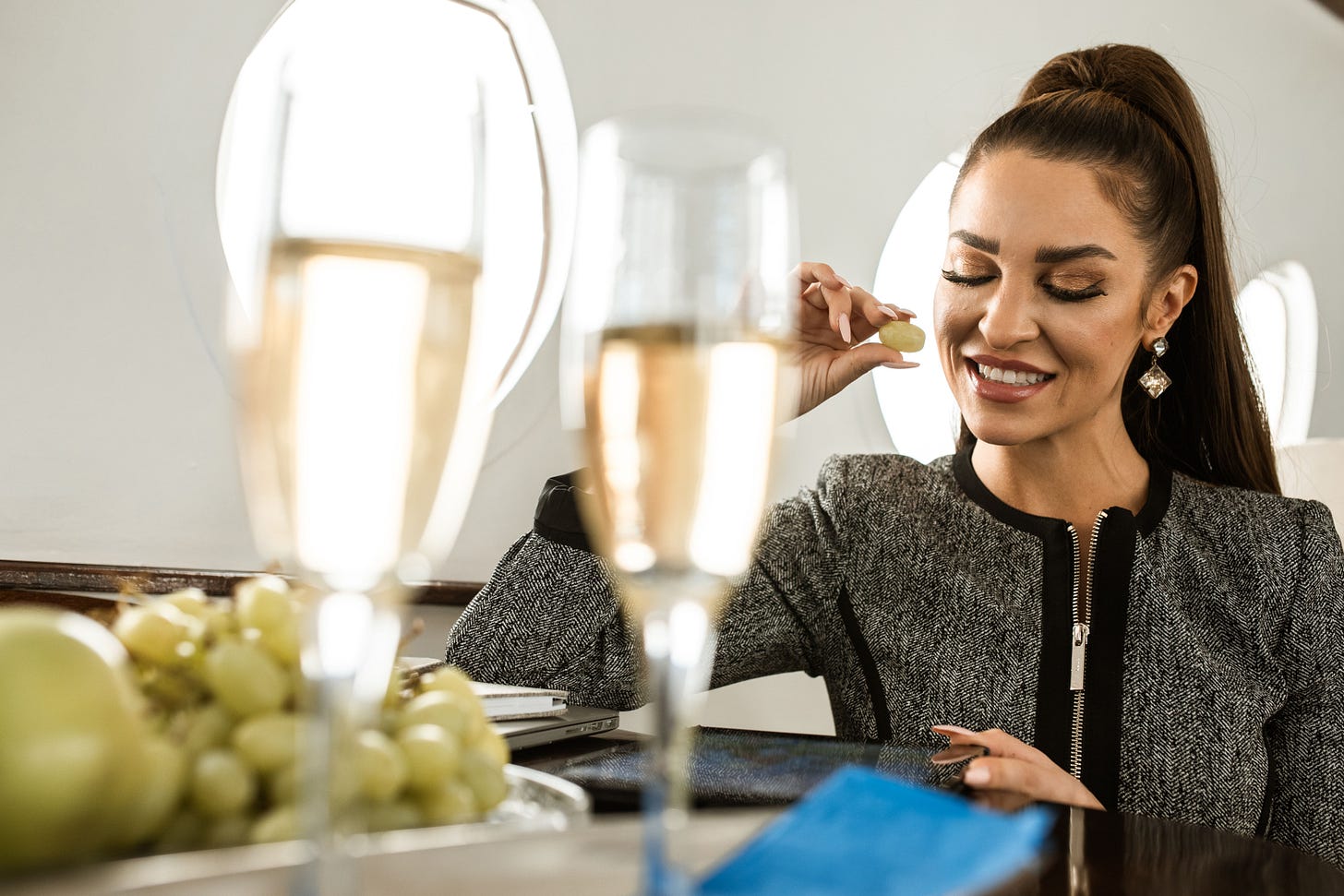 Rich woman sitting in a private aeroplane eating green grapes from a bowl next to a glass of champagne 