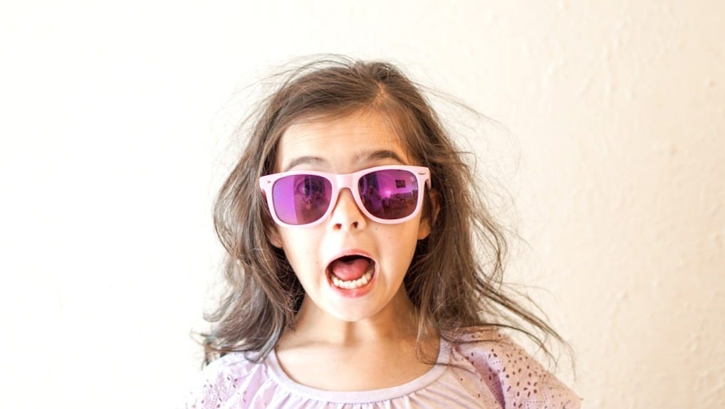 girl in white and purple floral crew neck shirt wearing blue framed sunglasses
