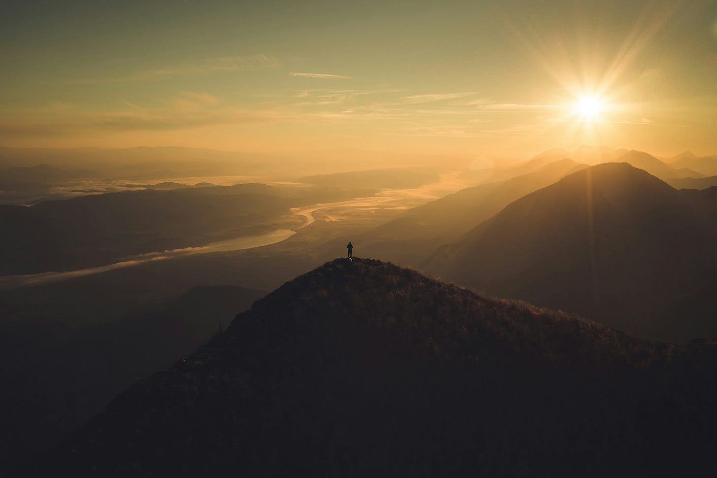 Person on the mountains at sunrise on top of the hill with river and fog in the valley.