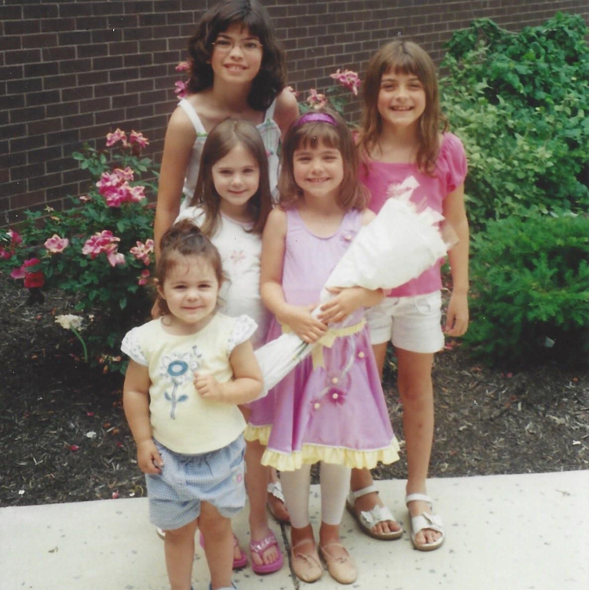Two school-aged sisters and two preschool-aged girl cousins posed with a preschool-aged girl after her dance recital