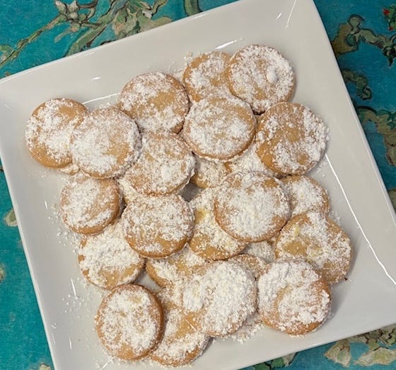 A plate of round walnut cookies dusted in confectioners sugar