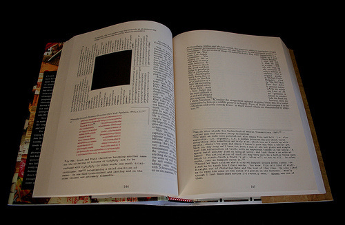 The book, House of Leaves, is open to a page with texts wrapping around a black square above stanzas written in red. In the adjacent page, text wraps around a blank square, with a footnote beneath it that takes up half the page. The book, House of Leaves, is open to a page with texts wrapping around a black square above stanzas written in red. In the adjacent page, text wraps around a blank square, with a footnote beneath it that takes up half the page.