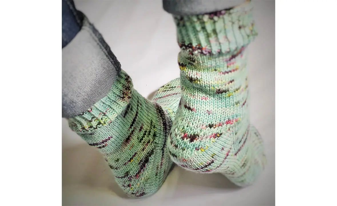 A close-up photograph of teal hand knitted socks with multi-colored speckles.