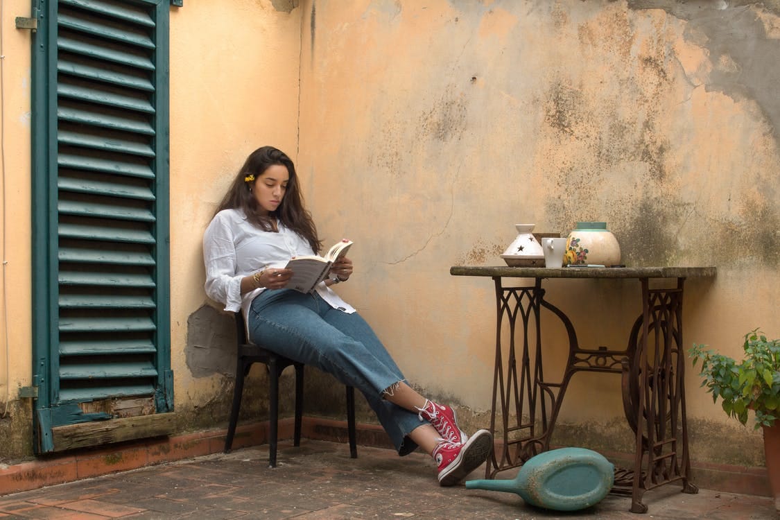 Woman in White Long Sleeve Shirt and Blue Denim Jeans Sitting on Black Wooden Seat