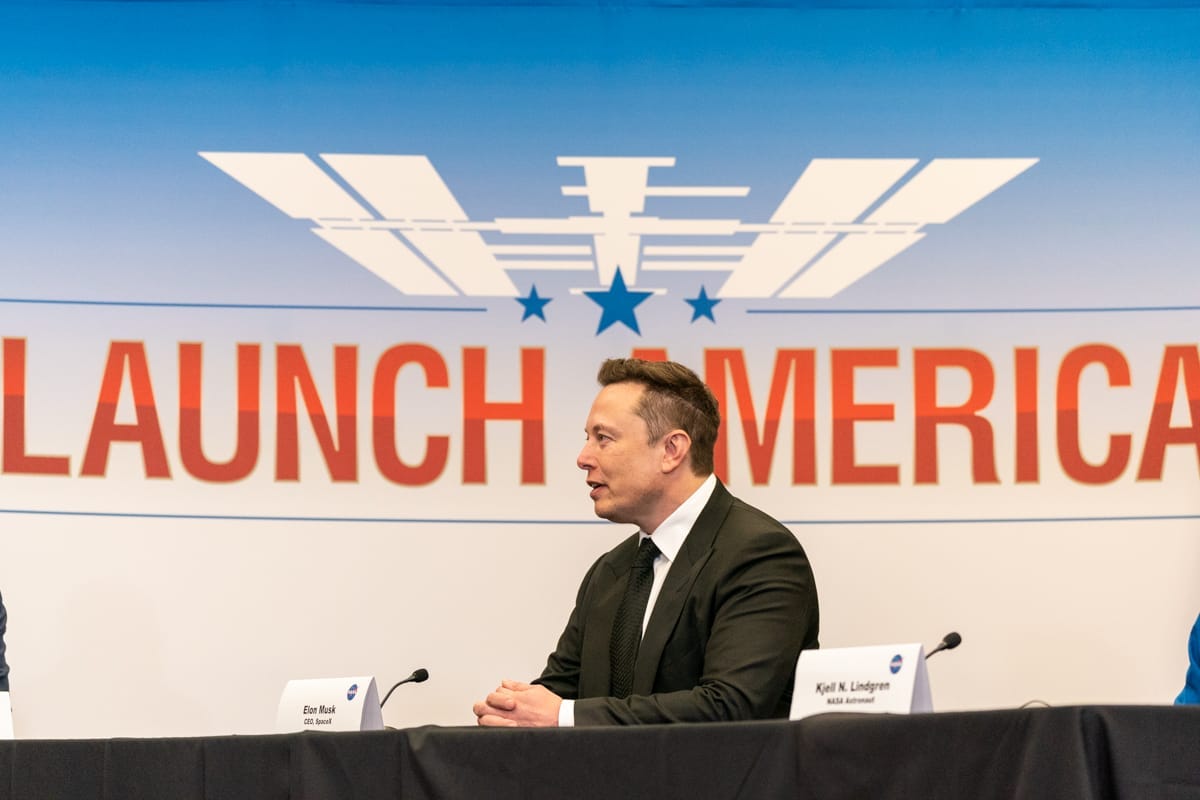 Elon Musk sitting in front of a graphic that says Launch America Elon Musk sitting in front of a graphic that says Launch America