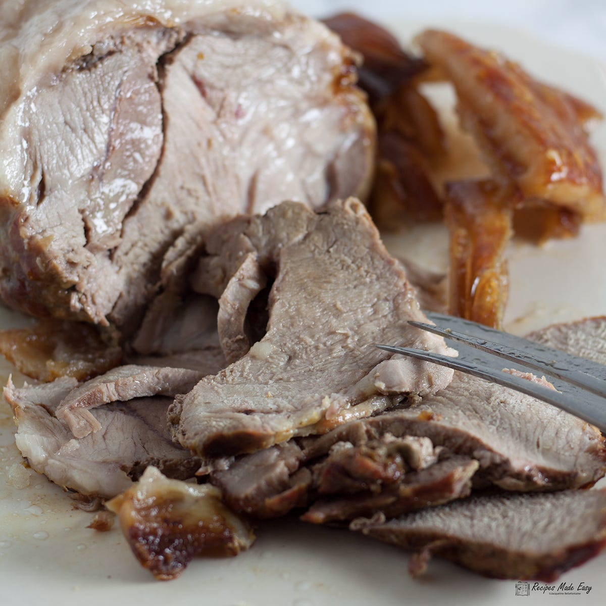Slices of roast pork in front of joint with crackling to the side.