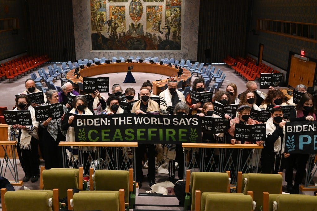 Dozens of Rabbis, all dressed in black stand behind a banner that reads: "Biden: the world says ceasefire" on the balcony of the United Nations Security Council Meeting Room