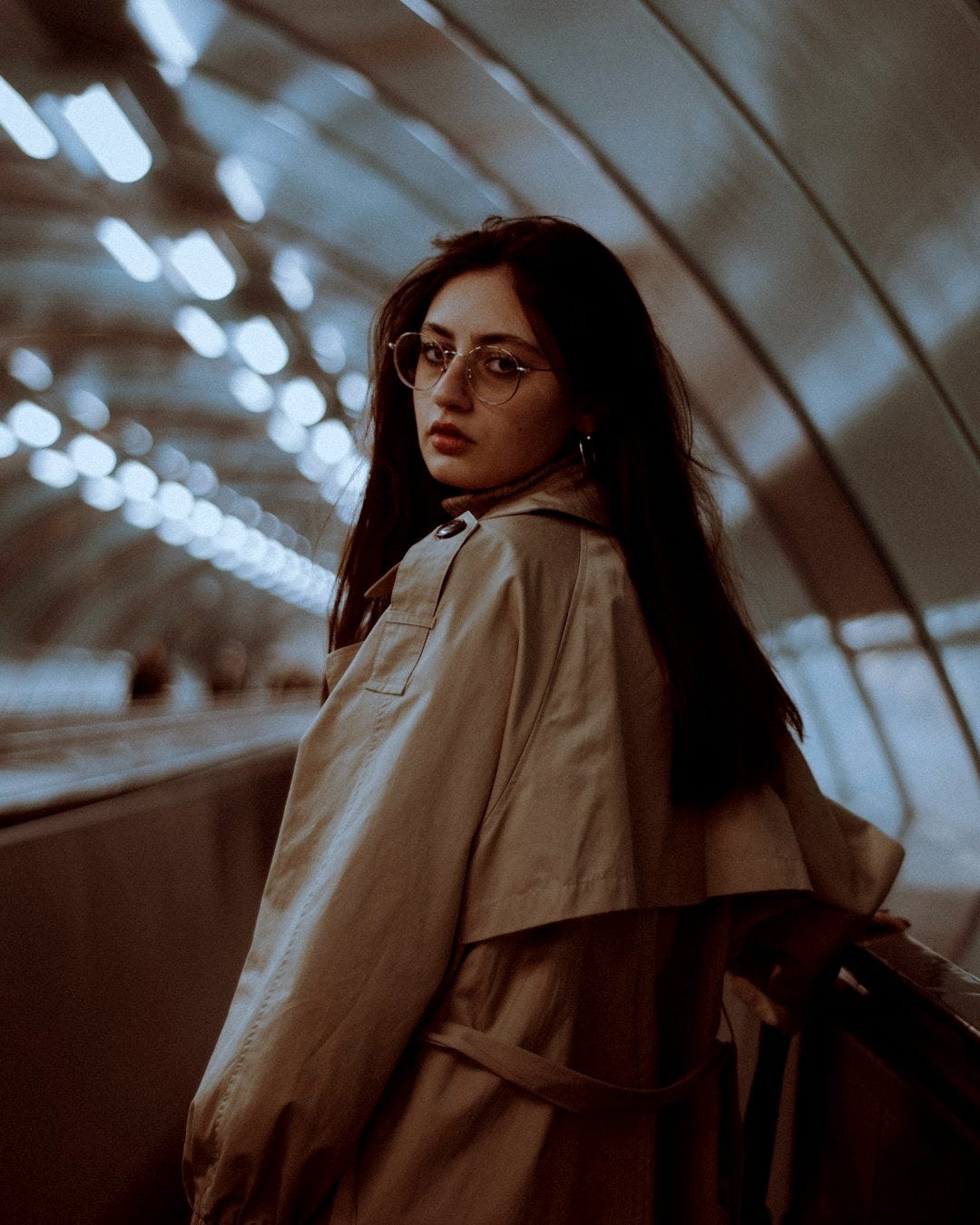 a woman in a trench coat standing in a subway station a woman in a trench coat standing in a subway station