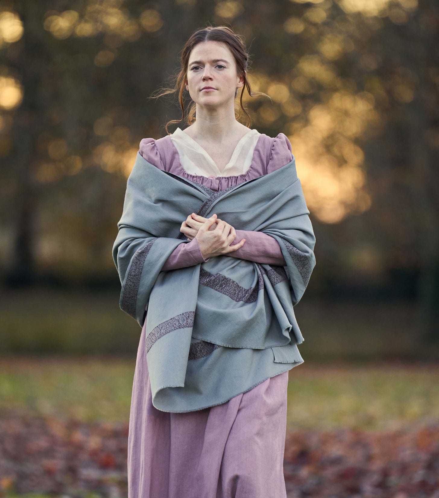 A young woman in Regency dress, her hair swept up in a knot, walks in an English landscape. It's a still featuring actor Rose Leslie from PBS Masterpiece's upcoming series 'Miss Austen' 
