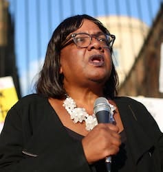 A black British politician called Diane Abbott addressing a crowd holding a microphone. A black British politician called Diane Abbott addressing a crowd holding a microphone.