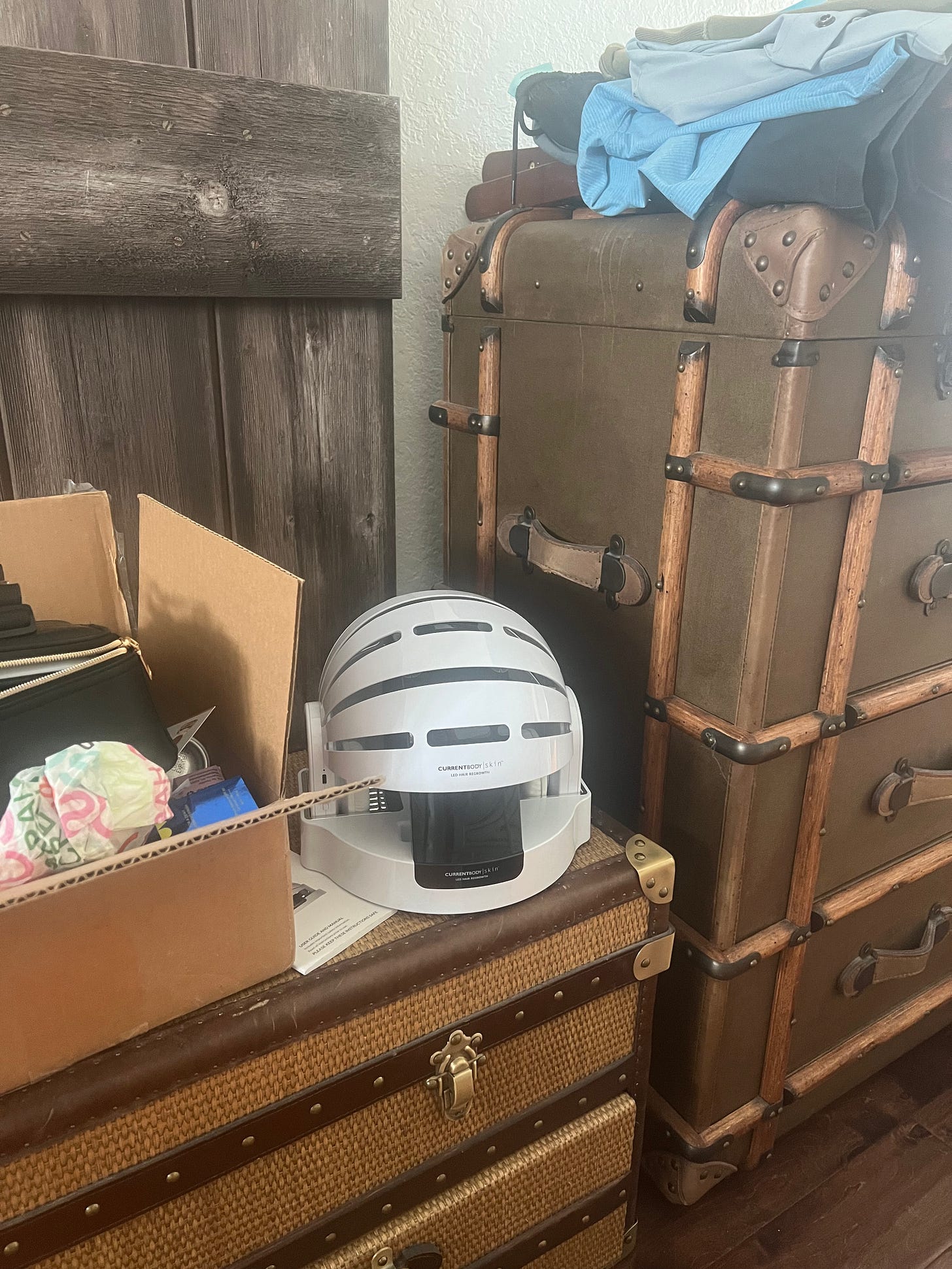 A red light hair helmet sitting on a bedroom trunk surrounded by laundry piles and work boxes. A red light hair helmet sitting on a bedroom trunk surrounded by laundry piles and work boxes.