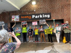 Group of protesters holding protest sign in front of an ICON parking sign