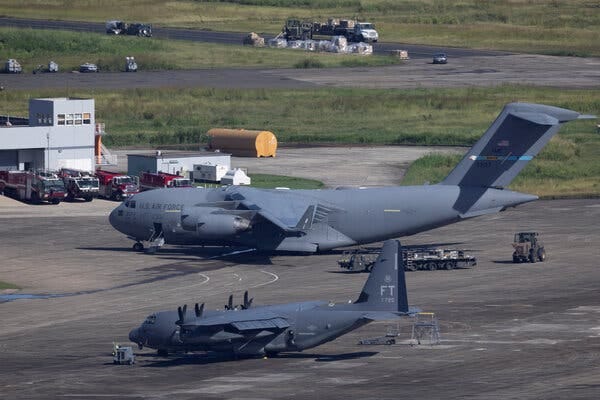 A very large gray U.S. military aircraft sits on the tarmac, next to a smaller gray military aircraft. 