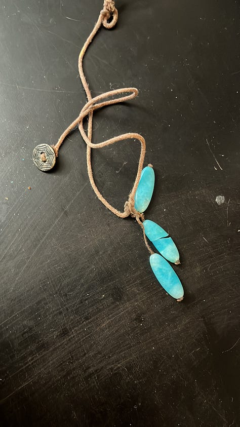 A black figurine of an Egyptian cat. A road lined with blossoming cherry trees. A necklace of aqua colored stones that are cracked and broken. An empty seat and rainy window at a cafe, with coffee on the table. An ikebana arrangement of tall daffodils. A campfire burning inside a potbellied chiminea. A collection of art supplies and a plaster angel. A watercolor sketch of cartoon spiders. A whiteboard at my job bearing the question, What's Your Favorite Thing About Baltimore In The Summer? With many many answers.