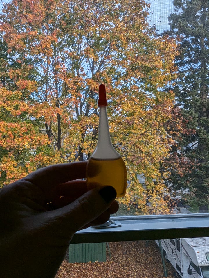 A photo on the left of a small (three inch?) bottle of oil, maybe 3/4 full. A photo on the right of a shiny white lady with her hair being blown back dramatically, wearing a very 1980s dolman-sleeve top with some sort of elaborate embroidery on it.