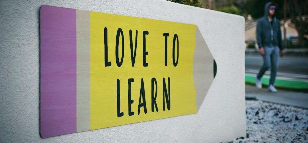 love to learn pencil signage on wall near walking man