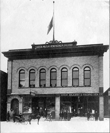 A black and white archival photograph of the original two-story Italian Hall building in Calumet before its demolition. It features a brick exterior and a prominent entrance.