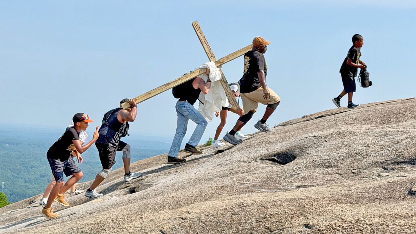 On July 4, Joseph Colt Hamrick (in blue jeans) loaded his two kids and a large wooden cross into his pickup truck and drove from Macon, Georgia, to the base of Stone Mountain. Hamrick said he was baptized two weeks earlier and felt the need to build the cross and carry it up a mountain. Hamrick carried it by himself much of the way before tiring and accepting help from two other men, including Shaun Quiovers (at front, in cap) and his children. On July 4, Joseph Colt Hamrick (in blue jeans) loaded his two kids and a large wooden cross into his pickup truck and drove from Macon, Georgia, to the base of Stone Mountain. Hamrick said he was baptized two weeks earlier and felt the need to build the cross and carry it up a mountain. Hamrick carried it by himself much of the way before tiring and accepting help from two other men, including Shaun Quiovers (at front, in cap) and his children.