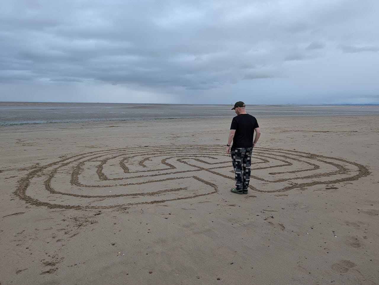 Someone contemplating a labyrinth drawn on the beach.