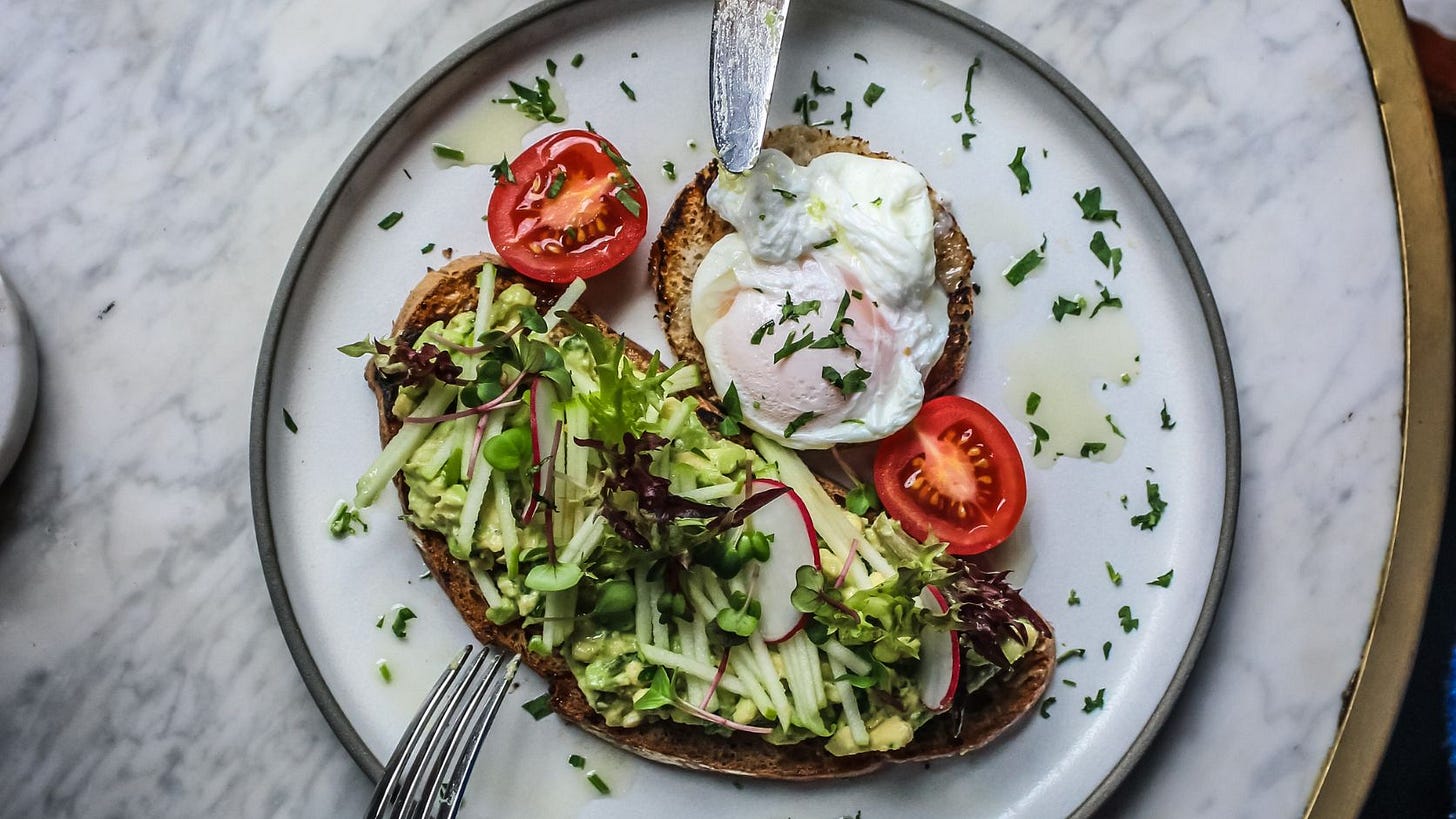 Healthy breakfast with avocado toast topped with fresh greens, radishes, cucumber, cherry tomatoes, and a poached egg on gluten-free toast, showing a balanced, nutrient-dense meal by nutrition stacking.