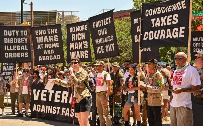 Estandartes de protesta con múltiples textos. Se lee "CONSCIENCE TAKES DUTY TO DISOBEY" (La conciencia impone el deber de desobedecer) y "END THE WARS AT HOME AND ABROAD " (Terminar con las guerras en casa y en el extranjero). Otras frases incluyen "NO MORE RICH MAN’S WARS" (No más guerras de ricos), "ICE OUT" (¡Fuera ICE!), "VETERANS AGAINST FASCISM" (Veteranos contra el fascismo) Estandartes de protesta con múltiples textos. Se lee "CONSCIENCE TAKES DUTY TO DISOBEY" (La conciencia impone el deber de desobedecer) y "END THE WARS AT HOME AND ABROAD " (Terminar con las guerras en casa y en el extranjero). Otras frases incluyen "NO MORE RICH MAN’S WARS" (No más guerras de ricos), "ICE OUT" (¡Fuera ICE!), "VETERANS AGAINST FASCISM" (Veteranos contra el fascismo)