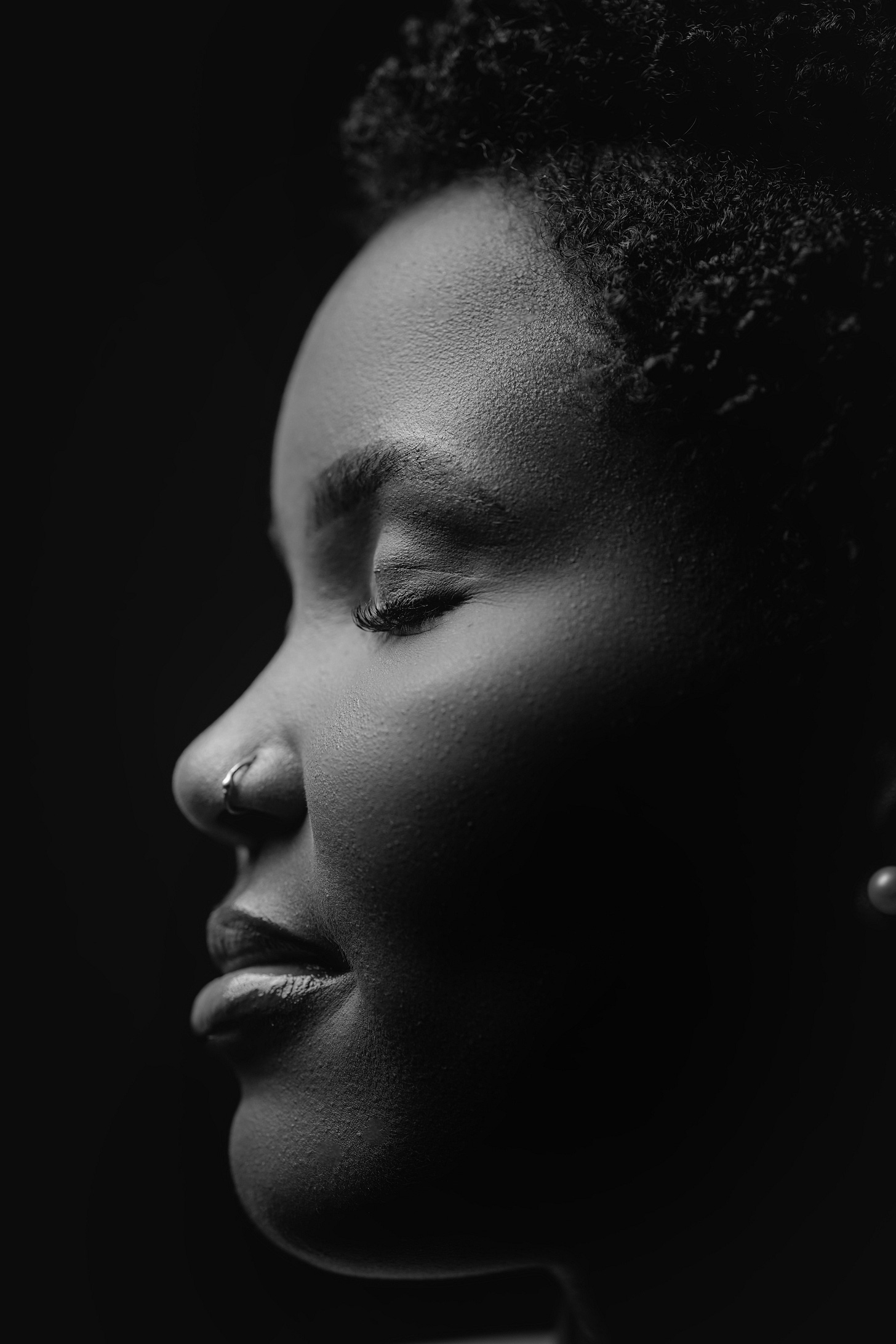 Black and white profile portrait of a Black woman with natural hair against a dark background, eyes closed in peaceful contemplation