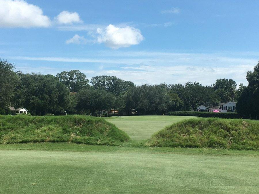 A golf course with trees and a blue sky

Description automatically generated